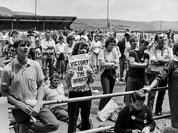Miners' supporter Vi John holds an iconic poster at a fundraising rally. Maesteg, July 1984